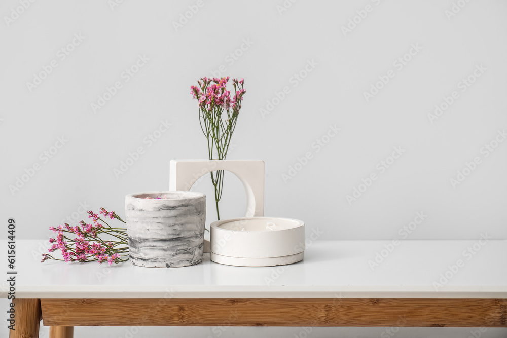 Beautiful flowers and candles on table near light wall in room