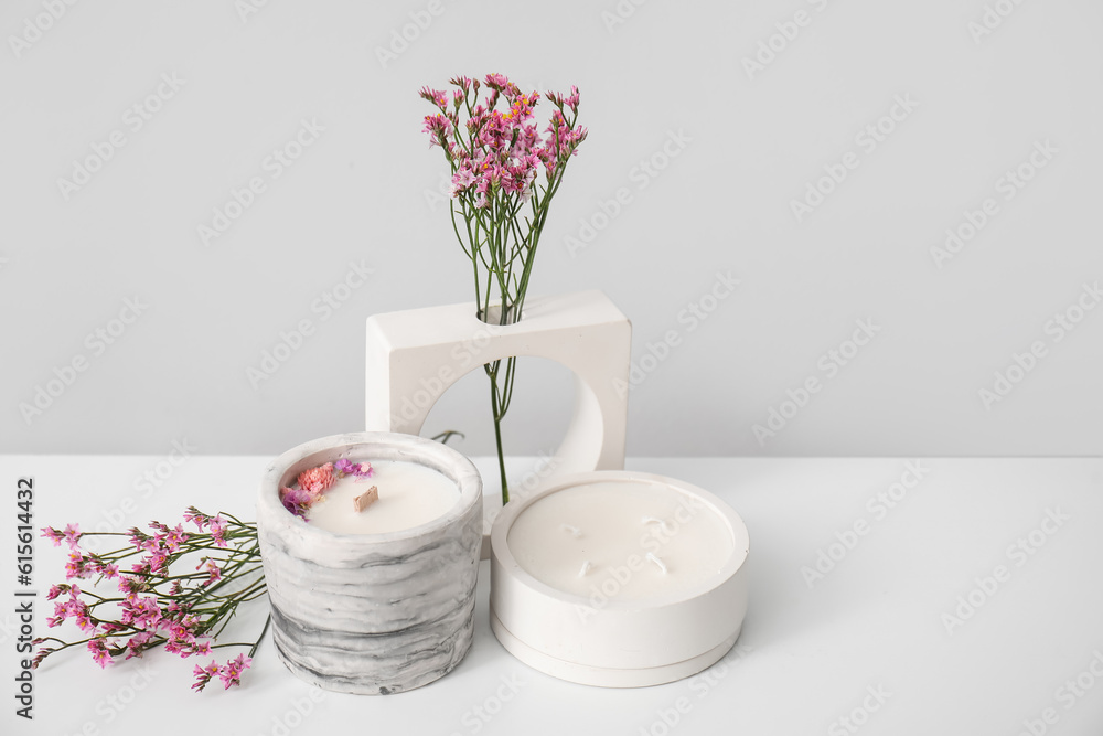 Beautiful flowers and candles on table near light wall in room, closeup