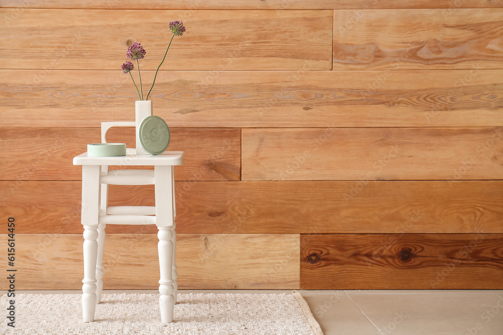 Beautiful flowers and candle on chair near wooden wall in room