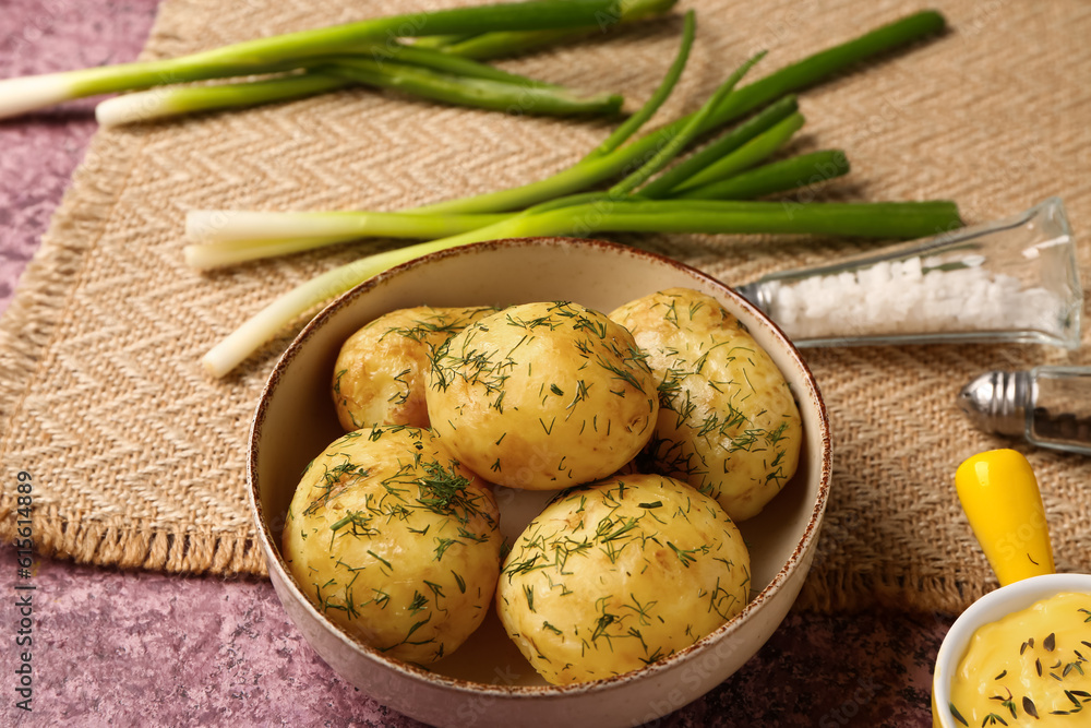 Plate of boiled baby potatoes with dill and sauce on purple background