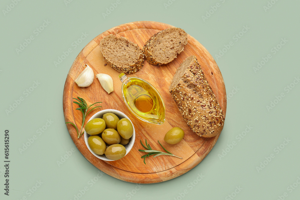 Bowl with ripe olives, bread and gravy boat of fresh olive oil on green background