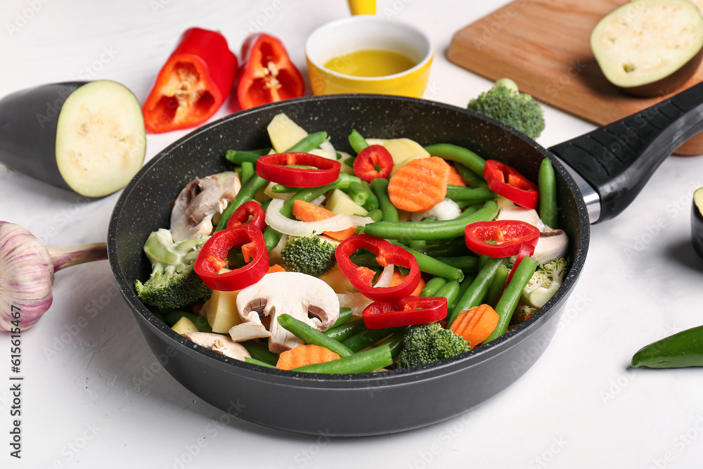 Frying pan with fresh vegetables on light background