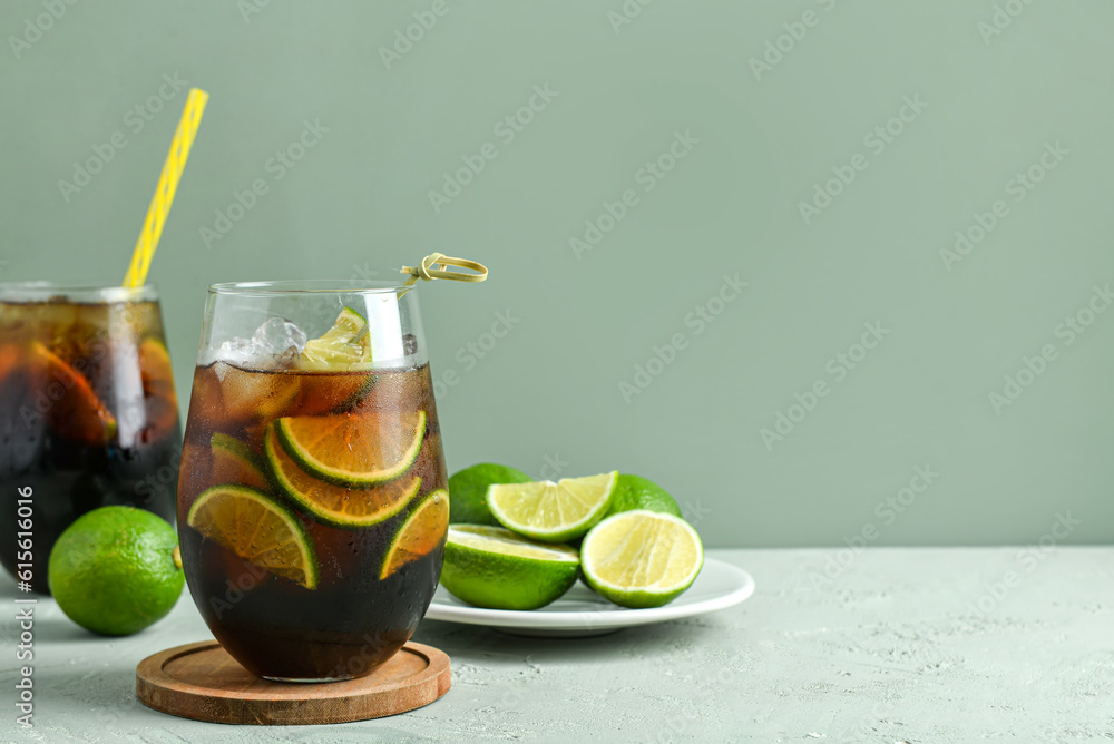 Glasses of cold Cuba Libre cocktail and plate with limes on grey background