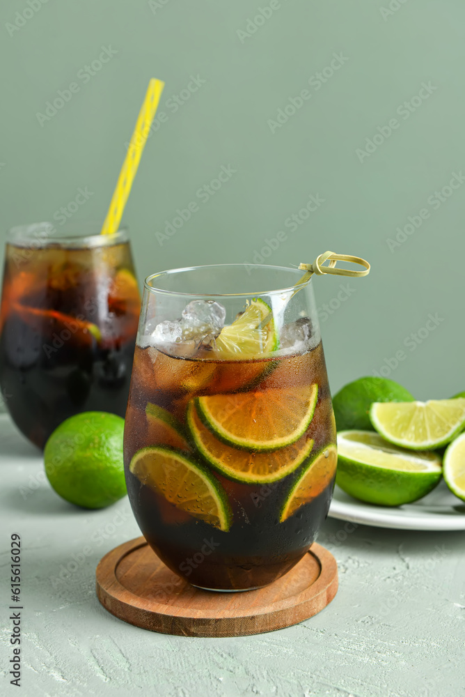 Glasses of cold Cuba Libre cocktail and plate with limes on grey background