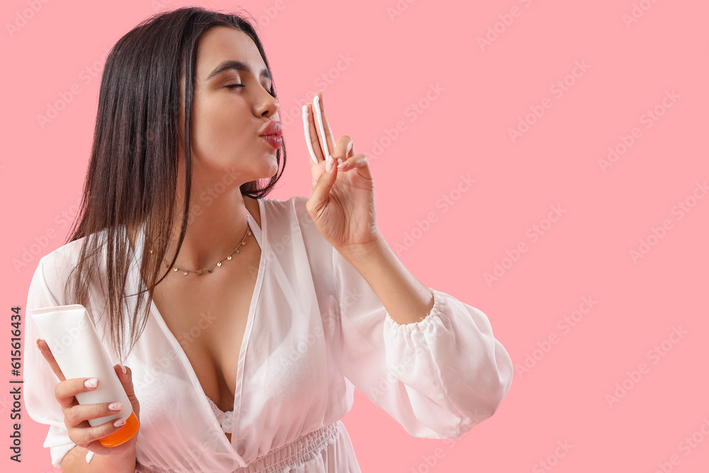 Young woman with sunscreen cream blowing kiss on pink background