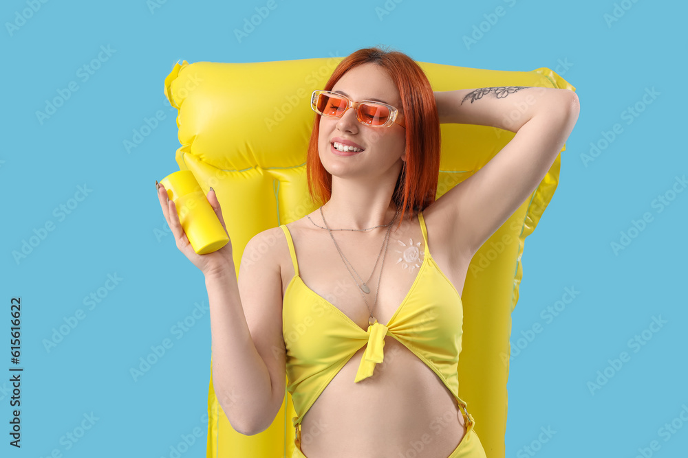 Young woman with sunscreen cream and inflatable mattress on blue background