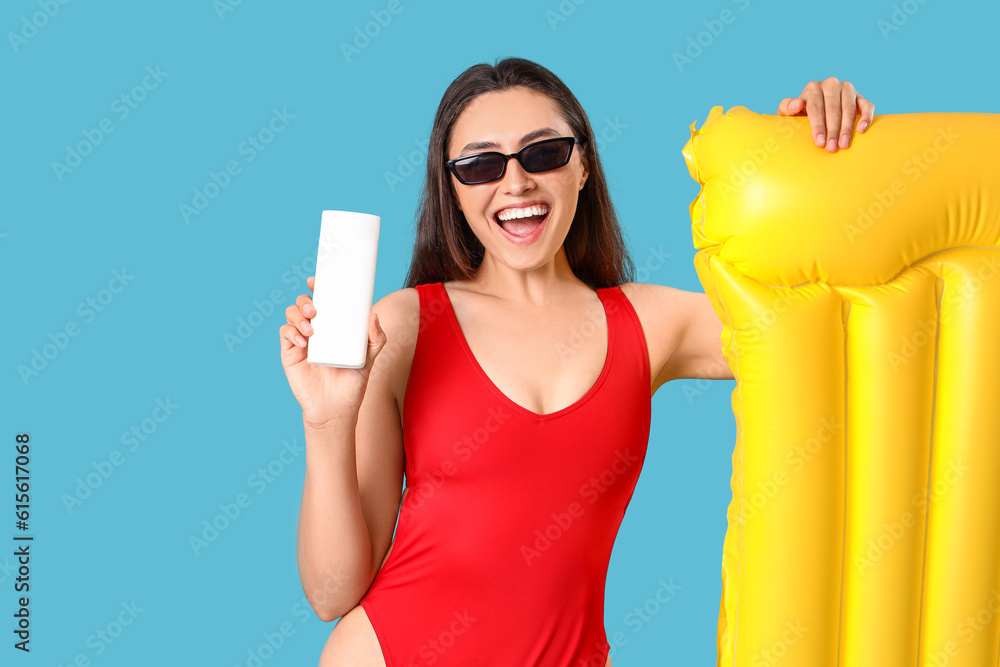 Young woman with sunscreen cream and inflatable mattress on blue background