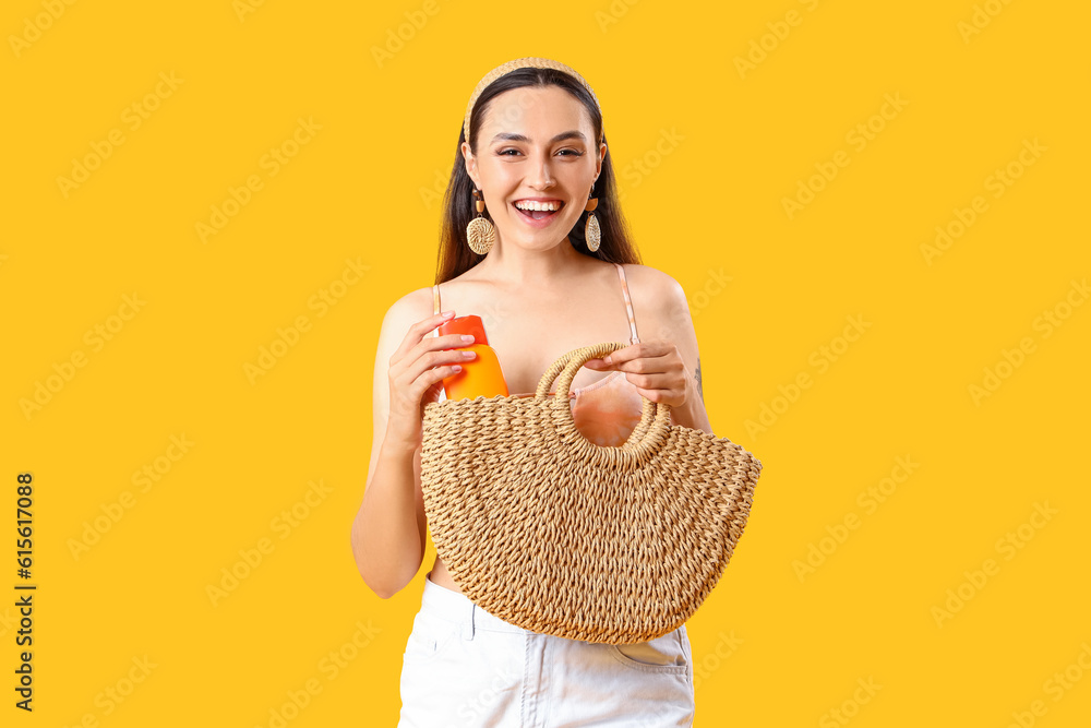 Young woman taking sunscreen cream out of beach bag on yellow background