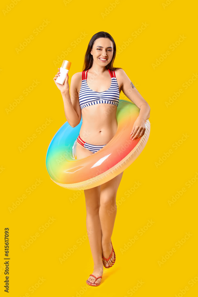 Young woman with sunscreen cream and inflatable ring on yellow background