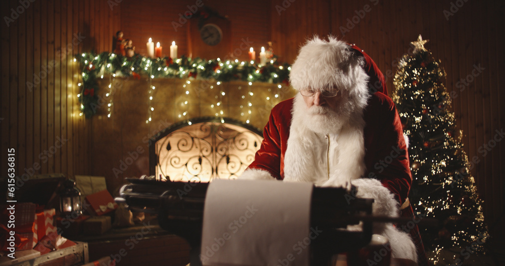 Senior bearded man in santa claus clothing is working on letter at his typewriter in christmas decor