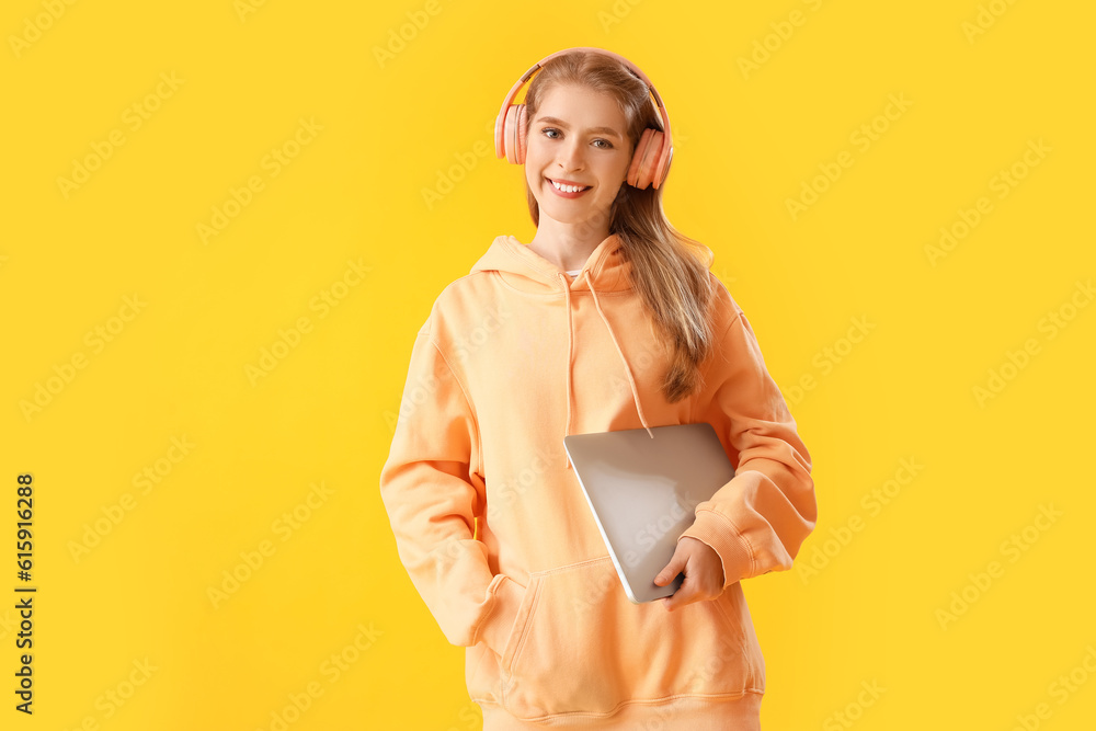 Female programmer in headphones with laptop on yellow background