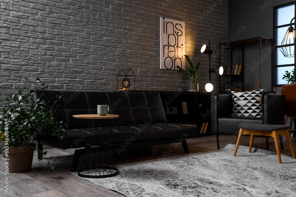 Interior of living room with black couch and glowing lamps in evening