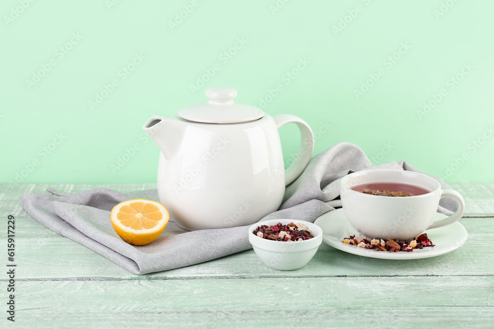 Cup of fruit tea, teapot and lemon on green wooden table