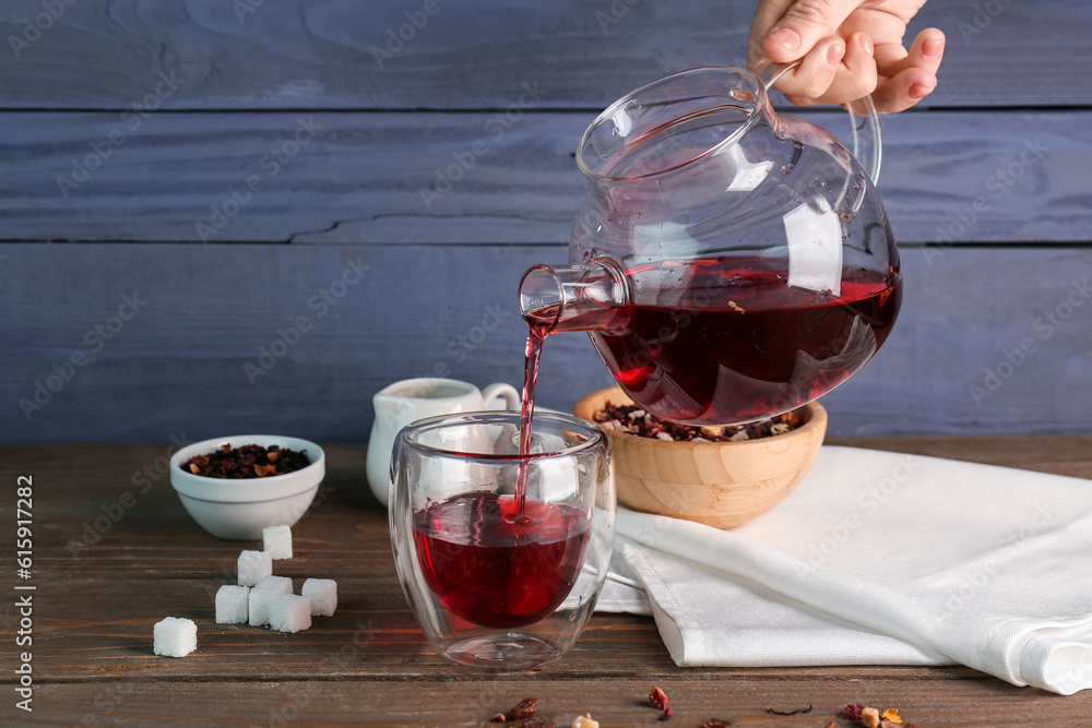 Woman pouring fruit tea from teapot into glass on wooden table