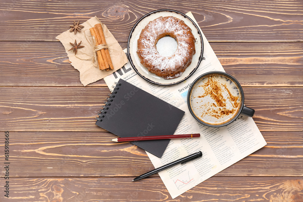 Cup of coffee with cake, cinnamon, notebook and newspaper on wooden background