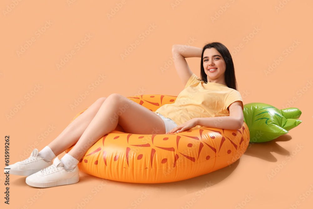 Young woman with inflatable ring lying on beige background