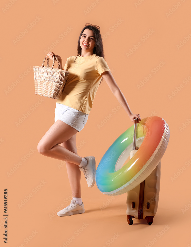 Young woman with beach bag, inflatable ring and suitcase on beige background