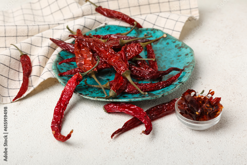 Plate with dry chili and bowl of sliced peppers on white background