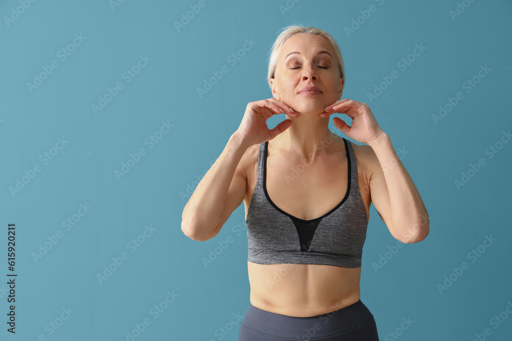 Sporty mature woman doing face building exercise on blue background