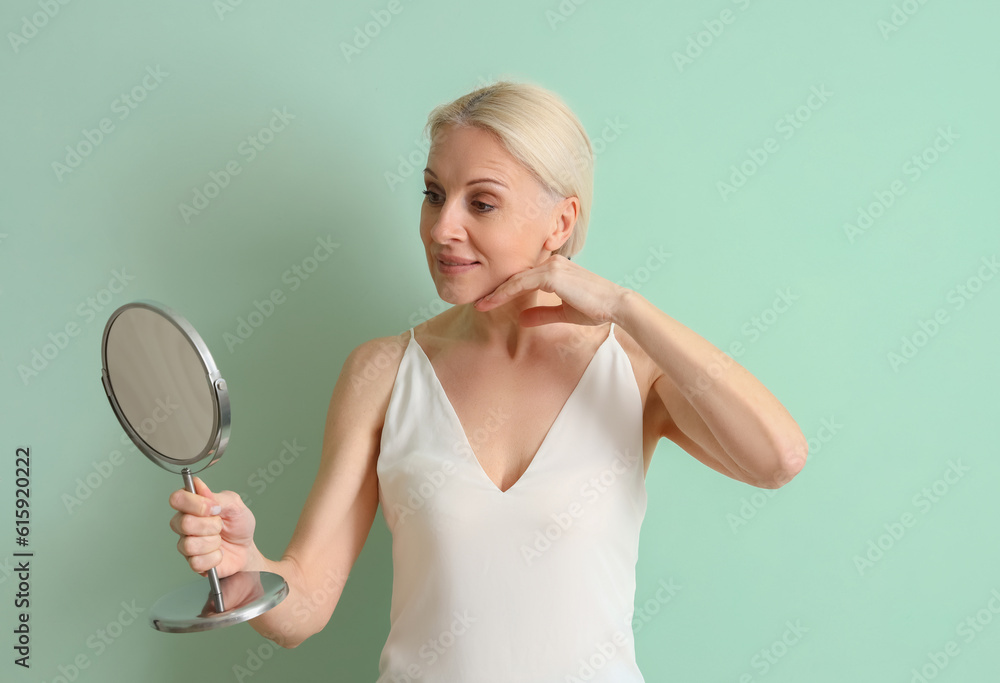 Mature woman with mirror doing face building exercise on green background