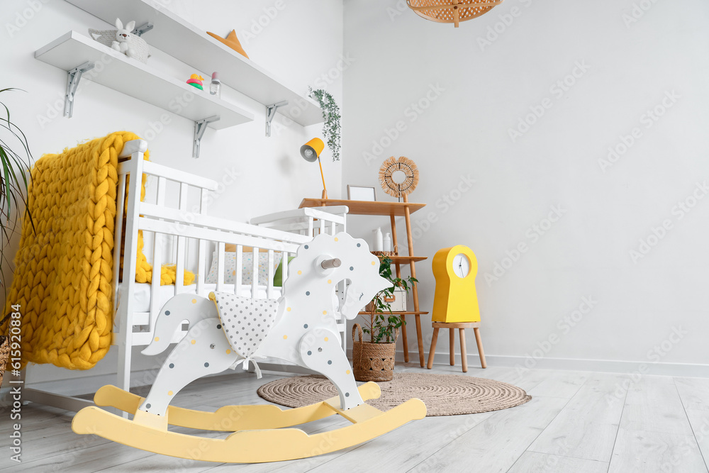 Stylish interior of childrens room with baby bed and rocking horse