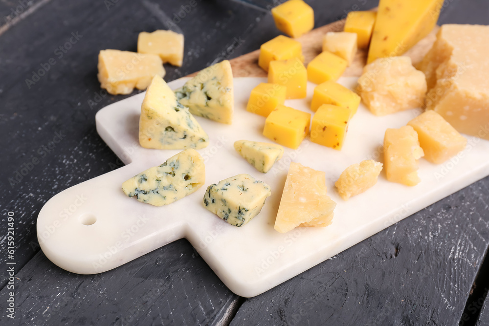 Board with pieces of tasty cheese on dark wooden background