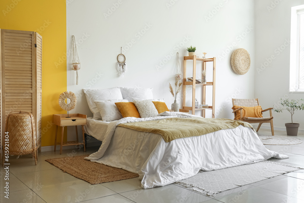 Interior of modern bedroom with bed, shelving unit and dream catcher hanging on white wall