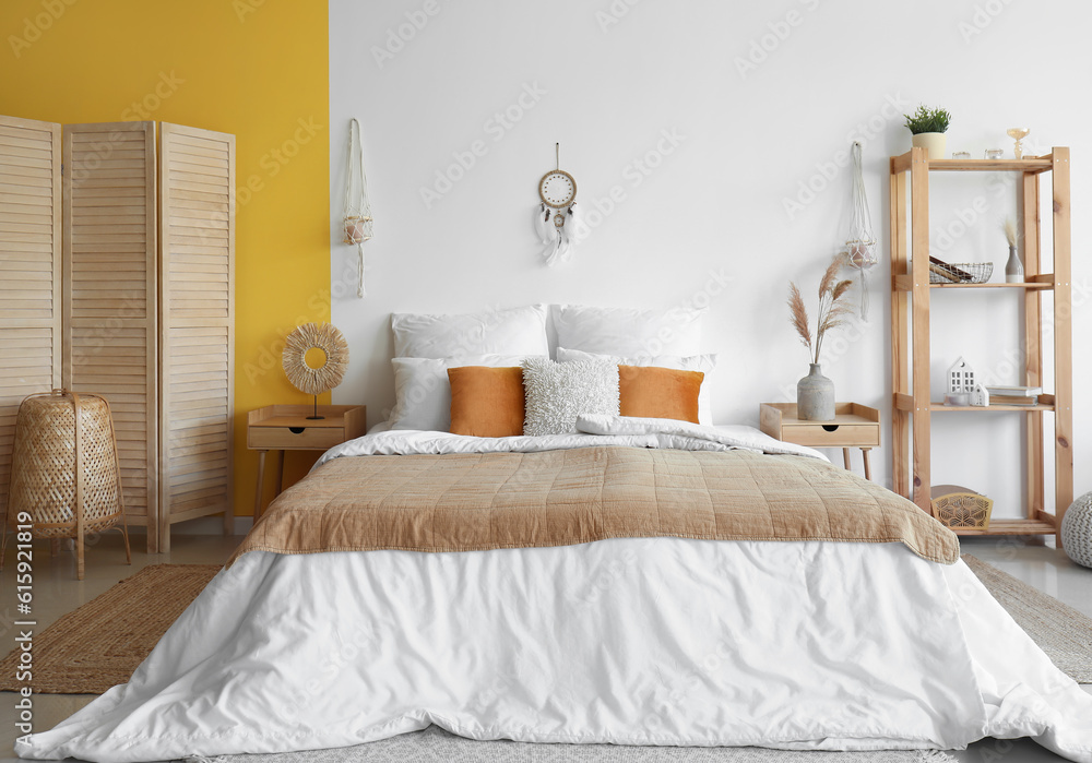 Interior of modern bedroom with bed, shelving unit and dream catcher hanging on white wall