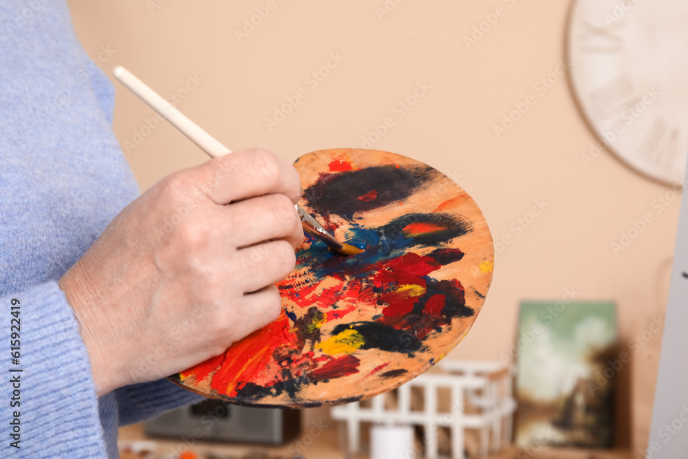 Mature female artist painting picture in  workshop, closeup