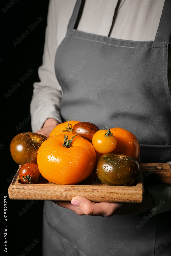 Woman holding wooden board with different fresh tomatoes on black background, closeup