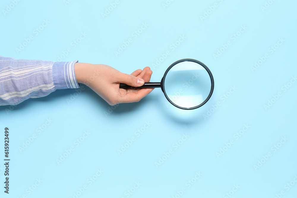 Female hand with magnifier on blue background