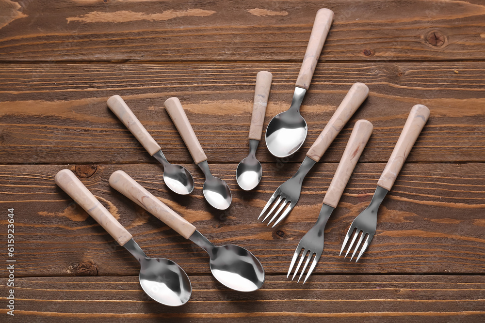 Stainless steel forks and spoons with plastic handles on wooden background