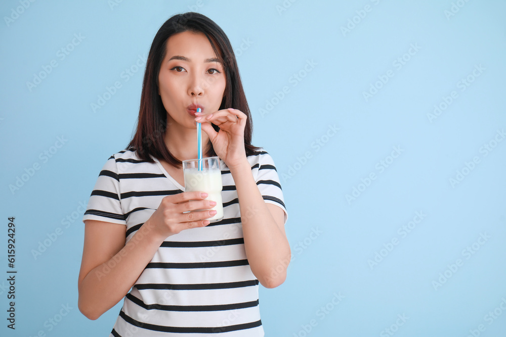 Beautiful Asian woman with glass of milk on light blue background