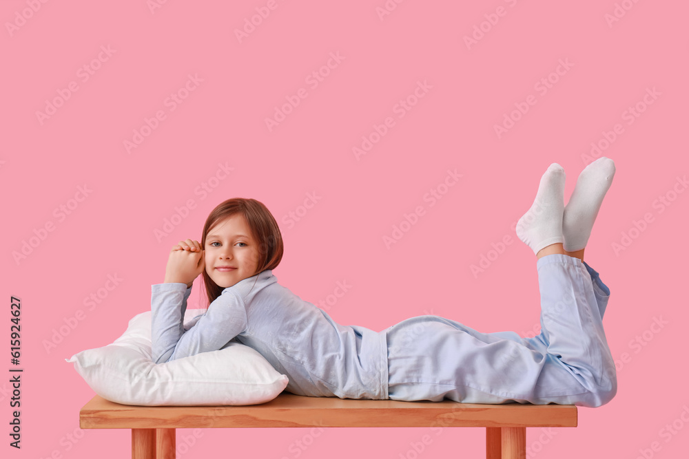 Little girl with pillow lying on bench against pink background