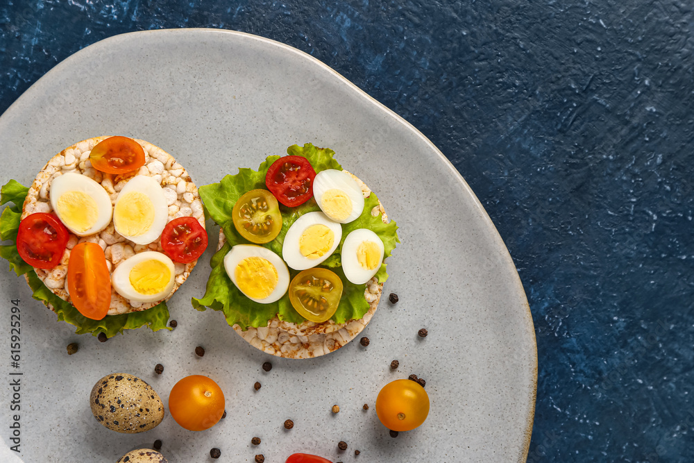 Rice crackers with quail eggs, tomatoes and lettuce on dark blue background