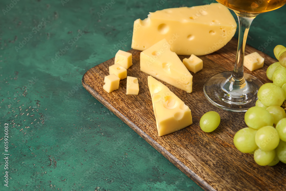 Wooden board with tasty Swiss cheese on green background