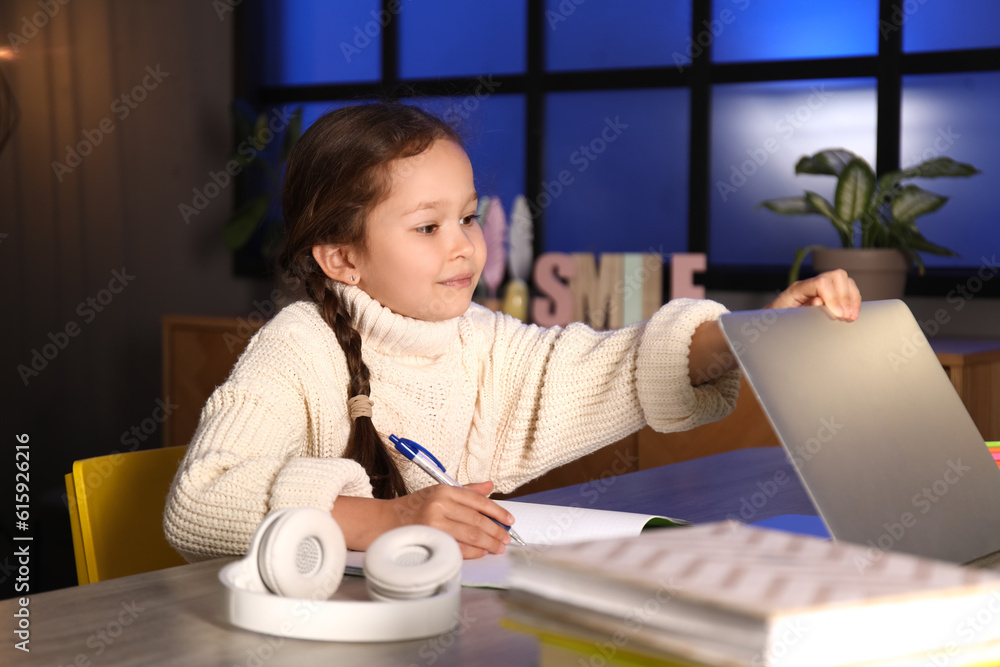 Little girl with laptop doing lessons at home late in evening