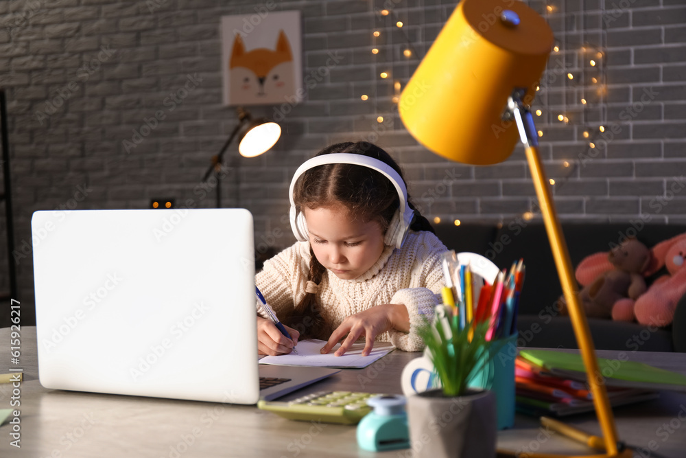 Little girl with laptop doing lessons at home late in evening