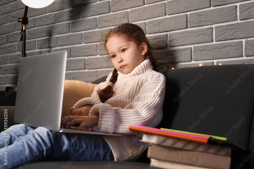 Little girl with laptop doing lessons at home late in evening