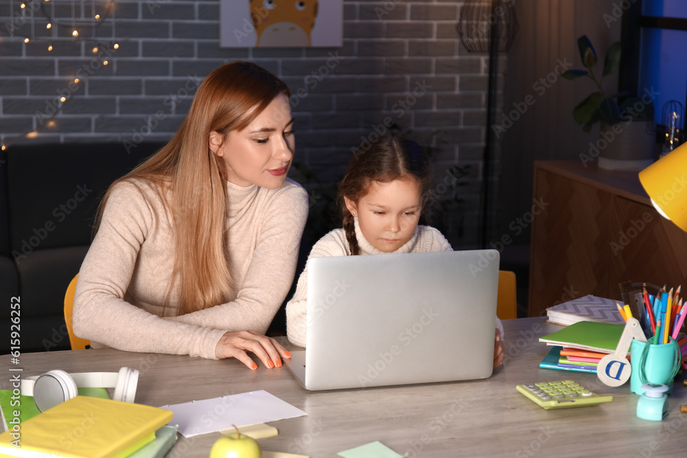 Little girl with her mother doing lessons at home late in evening