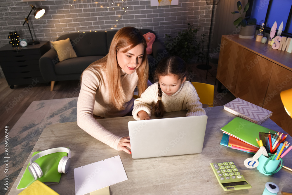 Little girl with her mother doing lessons at home late in evening