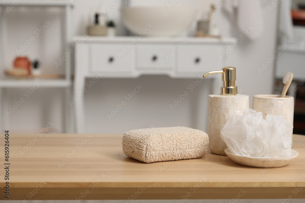 Soap dispenser, sponges and cup with toothbrush on wooden table in bathroom, closeup