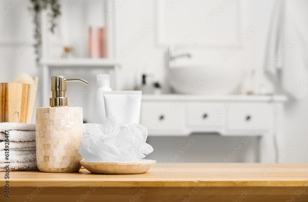 Soap dispenser, shower sponge, folded towels and bath accessories on wooden table in bathroom, close