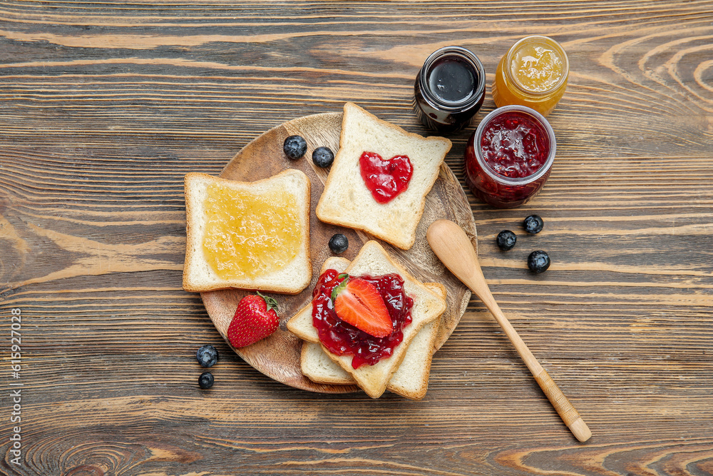 Plate with delicious toasts, jars of different jams and berries on brown wooden background