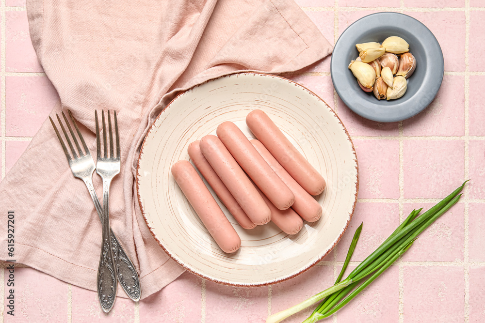 Plate with tasty thin sausages and garlic on pink tile background