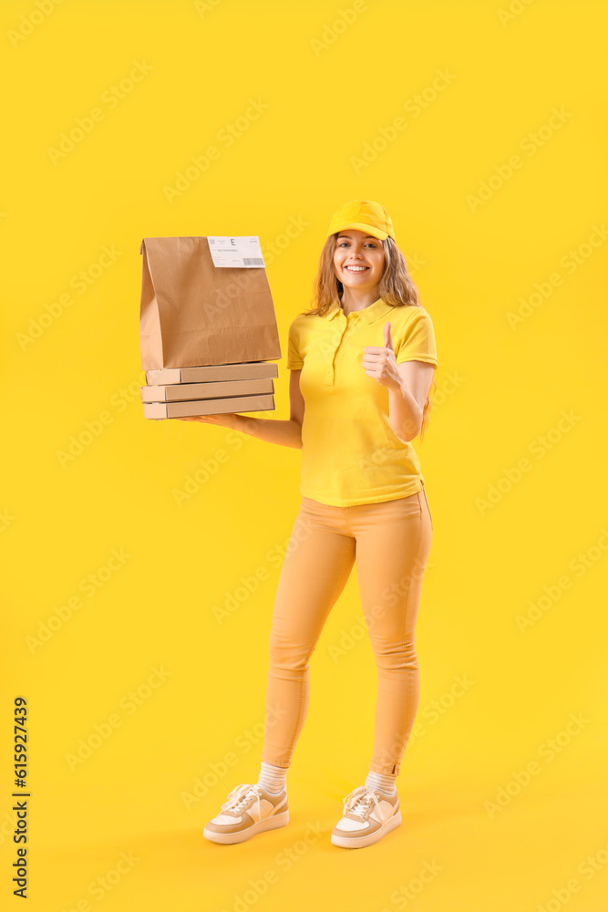 Female courier with paper bag and pizza boxes showing thumb-up on yellow background