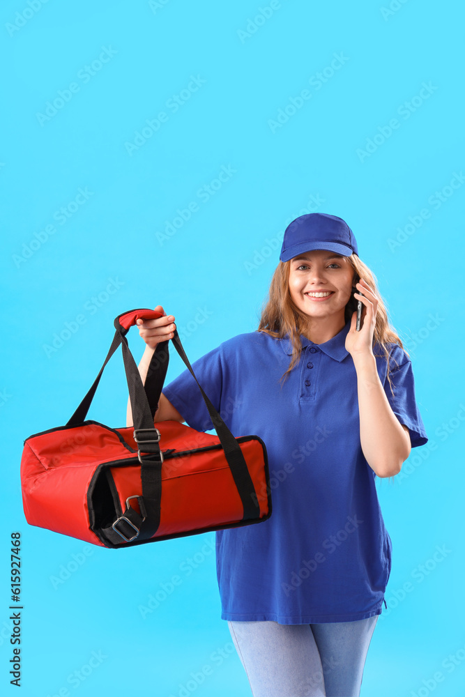 Female courier with thermal bag talking by mobile phone on blue background