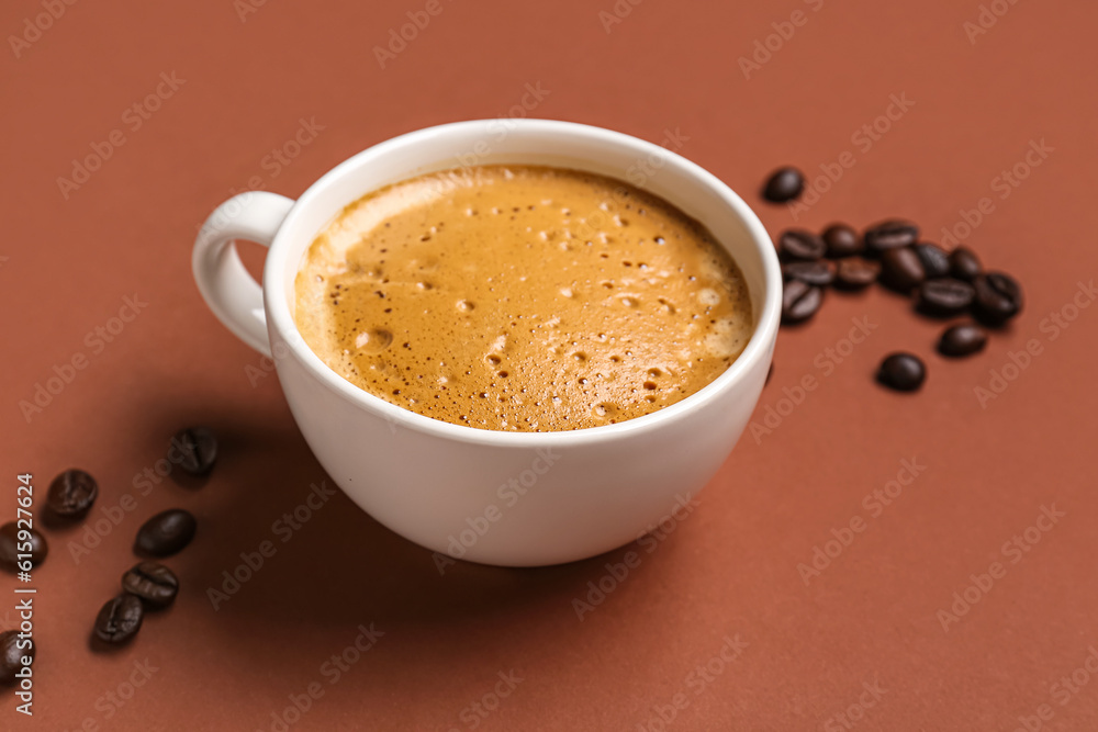 Cup of hot espresso and coffee beans on brown background