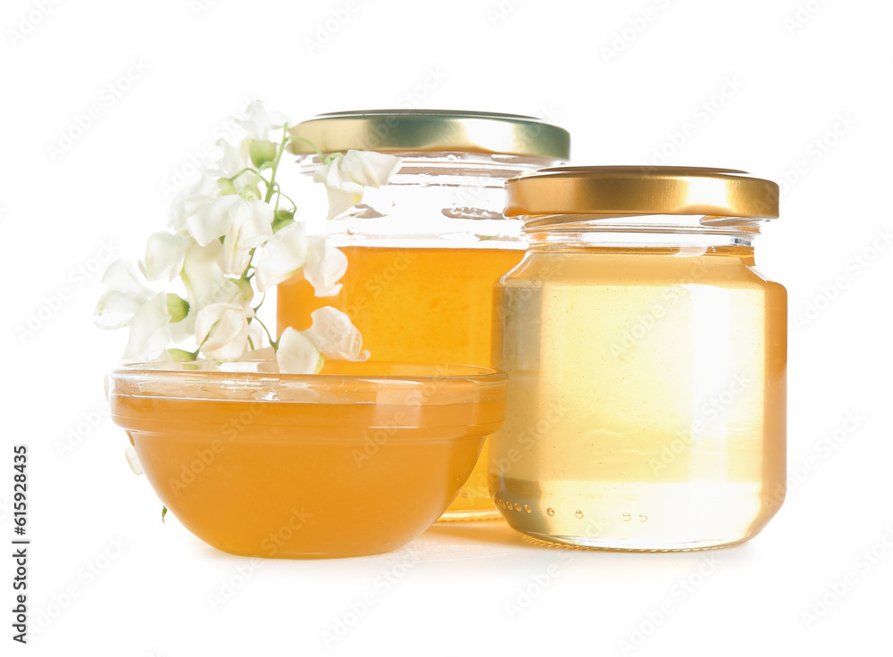 Jars and bowl of honey with flowers of acacia on white background