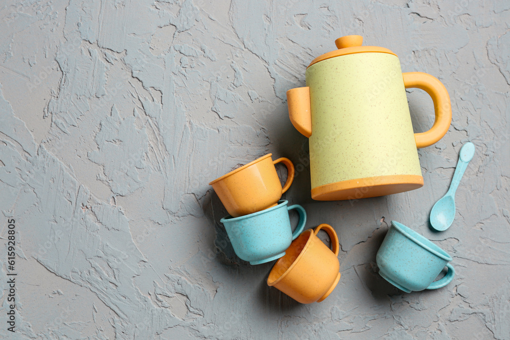 Teapot with cups and spoon for baby on grey background